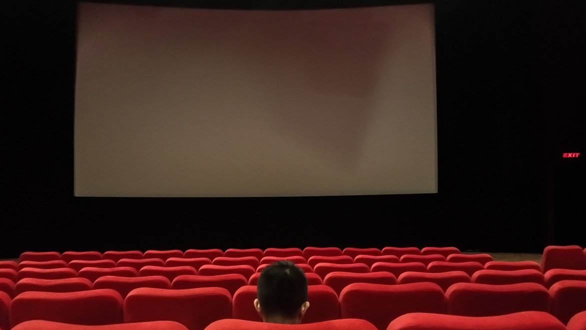 Seorang penonton sedang duduk di dalam studio bioskop.