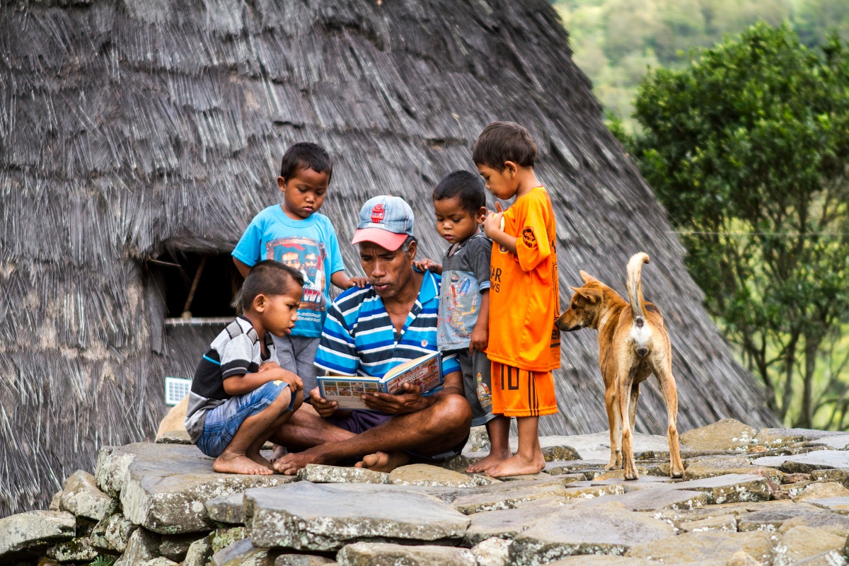 Seorang bapak warga Desa Wae Rebo membacakan cerita pada anak-anak.